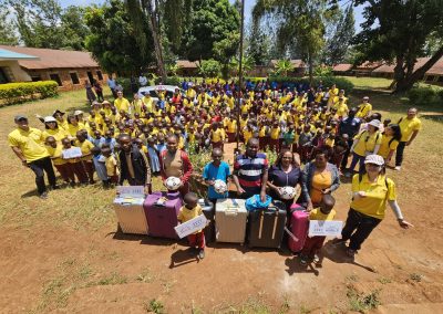 A group of kids from Mukangu Primary School and the visiting team standing with six suitcases of gifts for the school